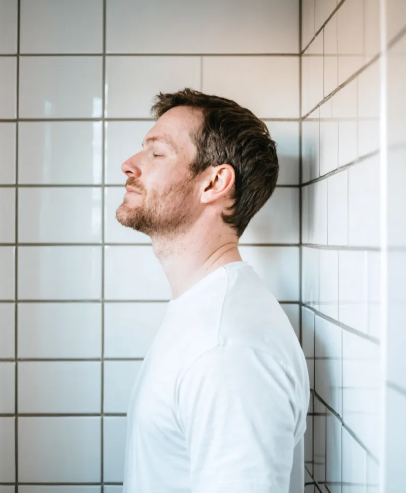 Man i profil med slutna ögon mot vitt kakel